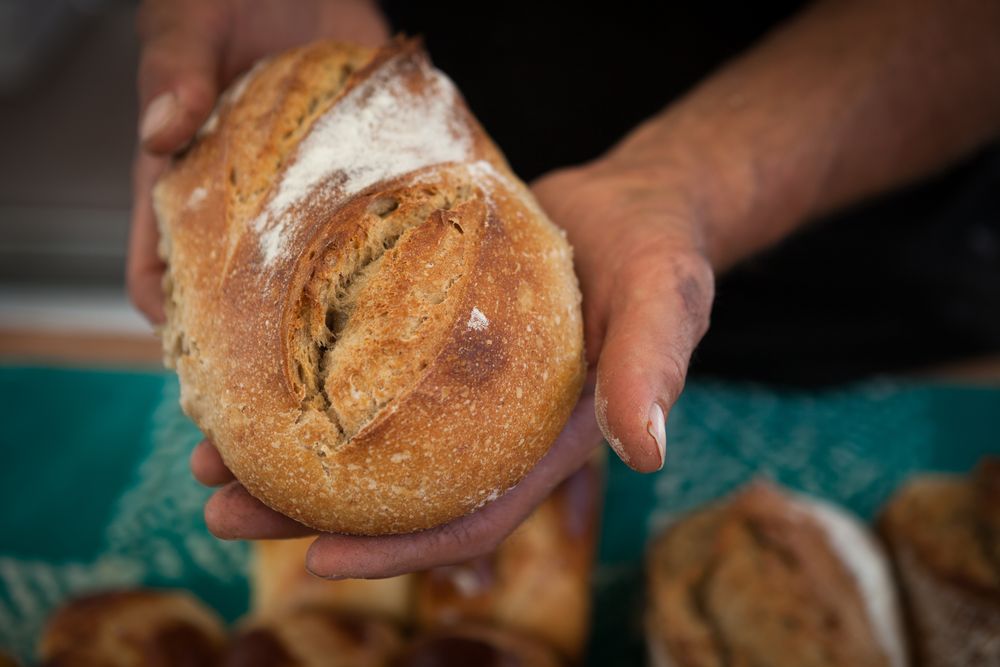 Deux mains tendent une miche de pain de campagne farinée